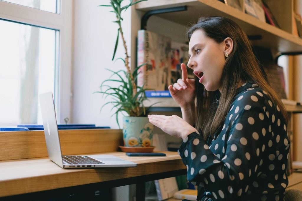 Young woman in a polka dot blouse using sign language during a video call at home.